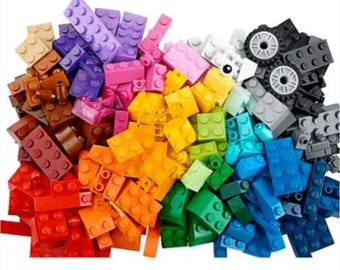May include: A vibrant assortment of colorful building blocks in various shapes and sizes. The blocks are in shades of red, orange, yellow, green, blue, purple, and brown. Some black blocks with wheels are also present, suggesting a construction toy.