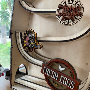 May include: A wooden farmhouse-style tiered shelf with three shelves. The top shelf has a brown circle with the text "The Labres Schmidtke Family". The middle shelf has a sunflower with the text "Bring Your Own Sunshine". The bottom shelf has a brown circle with the text "Farm Fresh Fresh Eggs Premium Quality".