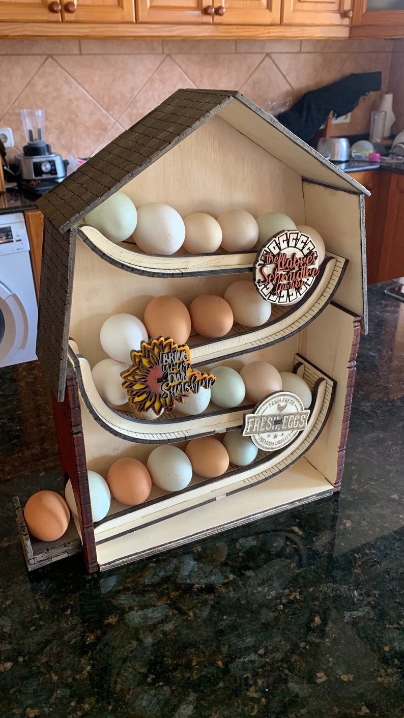 May include: Wooden farmhouse-shaped egg holder with four tiers. Each tier holds a row of brown and white eggs. The holder has three decorative signs: "The Labaree Schnauzer Family", "Bring Your Own Sunshine", and "Farm Fresh Fresh Eggs Premium Quality".