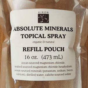 May include: A clear plastic refill pouch of Kiron Absolute Minerals Topical Spray. The label lists 16 oz. (473 mL) and ingredients including ocean-sourced magnesium chloride, seabed-sourced magnesium chloride hexahydrate, minerals, water, and iodine.