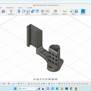 May include: A 3D model of a gray plastic phone holder with a slot for a phone and a stand for a charging cable. The holder has a series of holes on the side for cable management.