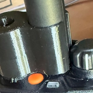 May include: Close-up of a black two-way radio with an orange button and a black antenna. The radio has a textured surface and a knob on the top. The radio is likely used for communication.