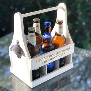 May include: A wooden beer carrier with a handle and a built-in bottle opener. It holds six bottles of beer and has the text "Daddy's Beers!!! Cheers Love Ronnie XXX" engraved on the side.