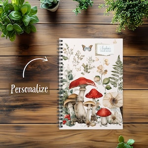 May include: Spiral-bound notebook featuring a watercolor illustration of mushrooms, flowers, and butterflies. The notebook has a cream-colored cover with the text "Sophia's Field Notes". The design includes red, brown, and white mushrooms.