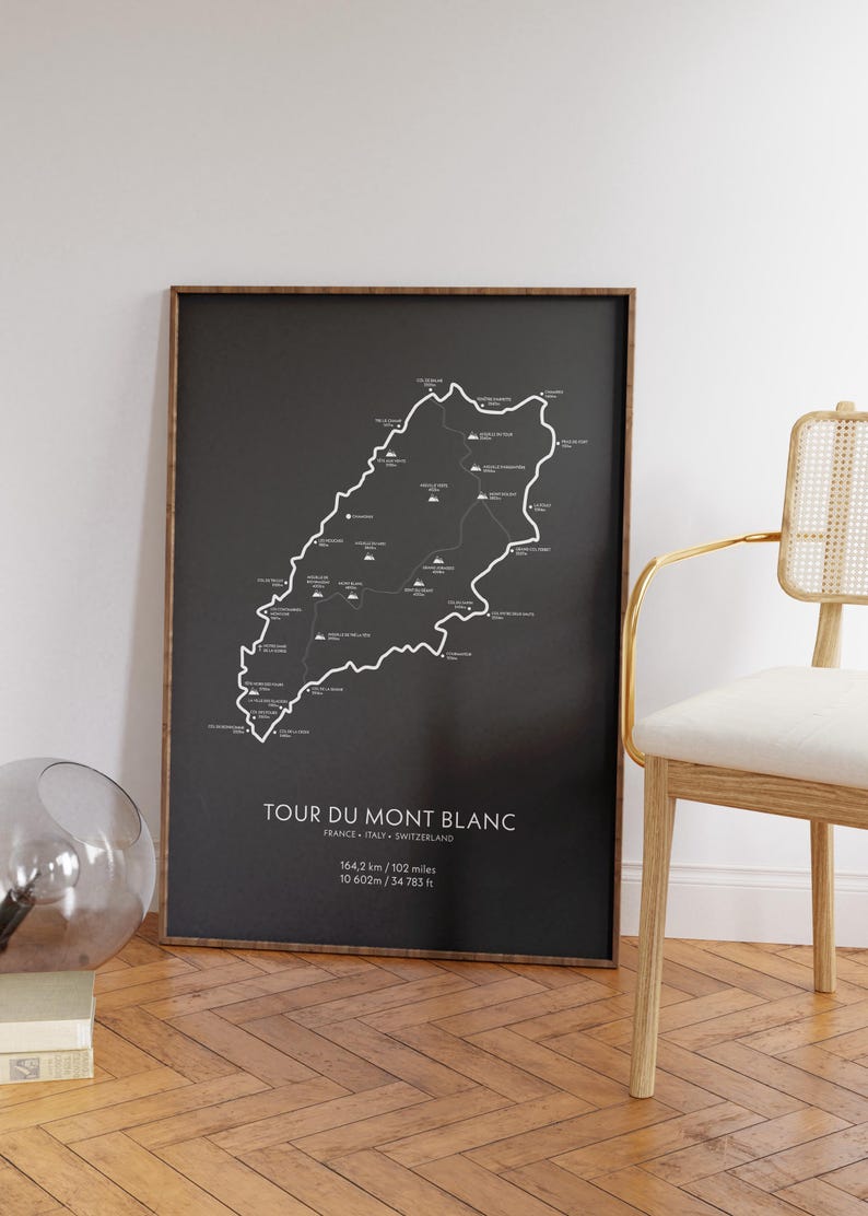 Może przedstawiać: Czarno-biały plakat z mapą szlaku Tour du Mont Blanc. Mapa pokazuje trasę szlaku, zmiany wysokości i kluczowe punkty. Tekst na plakacie brzmi "Tour du Mont Blanc, Francja - Włochy - Szwajcaria, 164,2 km / 102 mile, 10 602 m / 34 783 st&oacute;p."