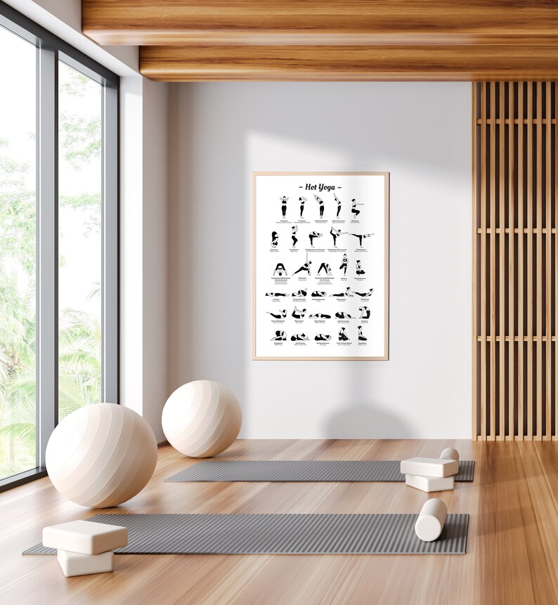 May include: A white framed poster with the title "Hot Yoga" and a black and white illustration of yoga poses. The poster is hanging on a white wall in a room with a wooden floor, two yoga mats, and a yoga ball.