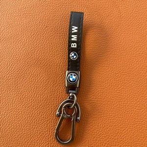 May include: A black leather keychain with a silver metal key ring and a BMW logo. The keychain has the word "BMW" printed in white on the leather strap.