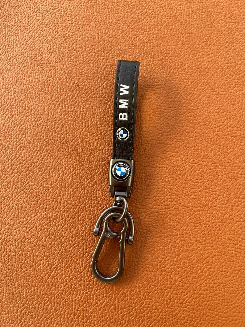 May include: A black leather keychain with a silver metal key ring and a BMW logo. The keychain has the word "BMW" printed in white on the leather strap.