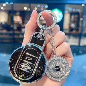 Peut inclure: Un porte-clés argenté avec un porte-clés Mini Cooper noir et argent et un charm rond argenté avec le mot "MINI" et des strass.