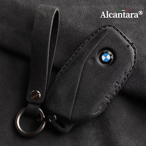 May include: Black leather key fob with a stitched edge and a silver BMW logo. The fob has a black leather strap with a silver ring.