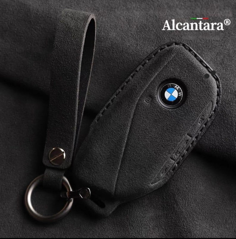 May include: Black leather key fob with a stitched edge and a silver BMW logo. The fob has a black leather strap with a silver ring.