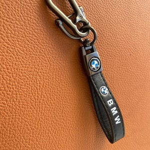 May include: A black leather keychain with a silver metal hook and a silver BMW logo. The keychain has the word "BMW" written on it.