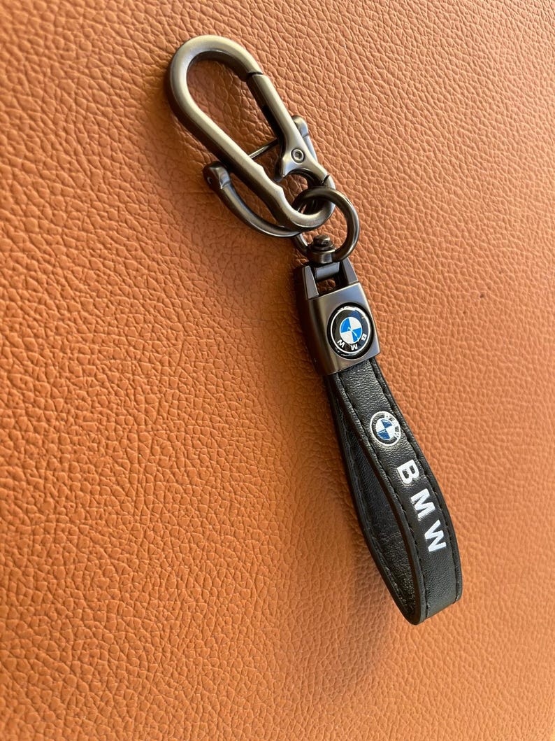 May include: A black leather keychain with a silver metal hook and a silver BMW logo. The keychain has the word "BMW" written on it.