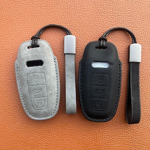 May include: Two leather key fobs with a wrist strap. One is grey and the other is black.