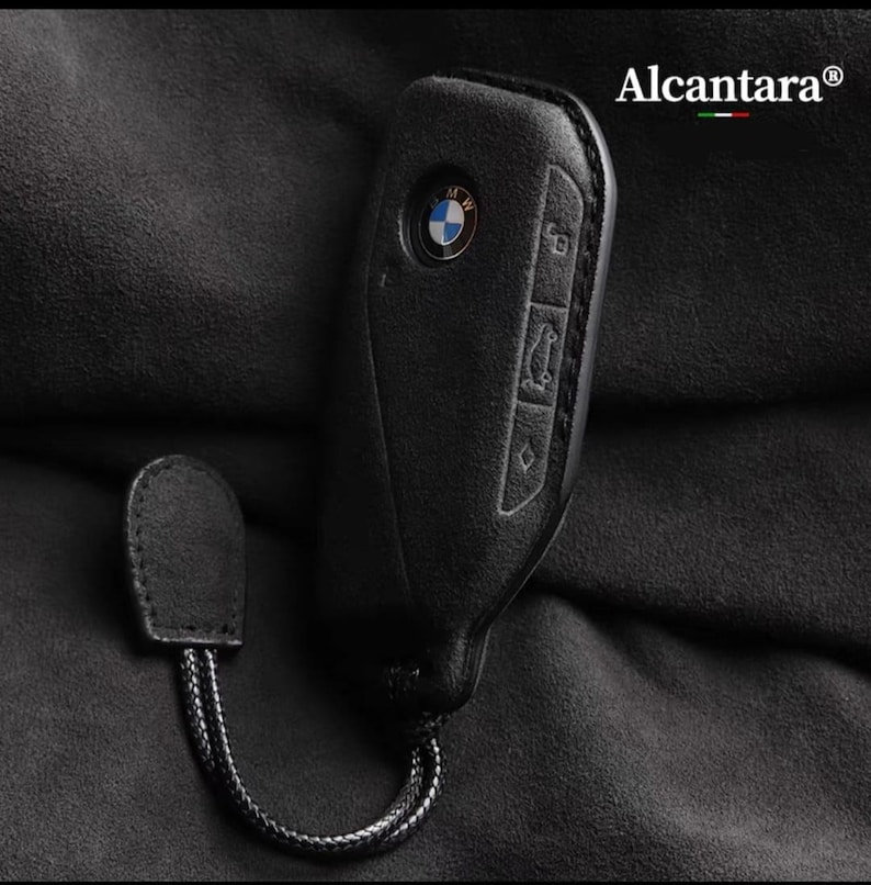 May include: Black leather key fob with a BMW logo and buttons. The fob has a black cord attached to it.