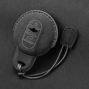 Può includere: Portachiavi in ​​pelle nera con una chiave grezza argentata e un cordino nero. Il portachiavi ha una superficie testurizzata e un piccolo anello per attaccarlo a un portachiavi.