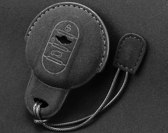 Op de afbeelding: Zwarte leren sleutelhanger met een zilveren sleutelblank en een zwart koord. De sleutelhanger heeft een gestructureerd oppervlak en een kleine lus om aan een sleutelring te bevestigen.