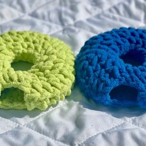 May include: Two crocheted donut-shaped pet beds, one in a bright green color and the other in a vibrant blue.