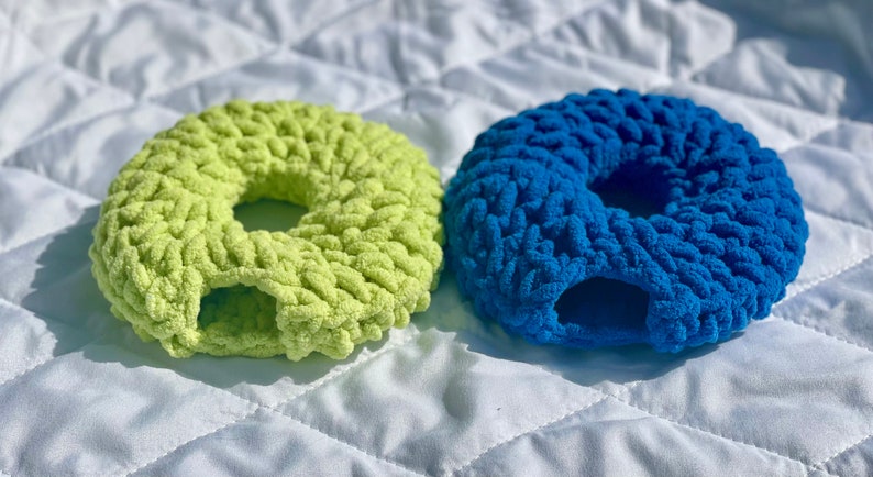 May include: Two crocheted donut-shaped pet beds, one in a bright green color and the other in a vibrant blue.
