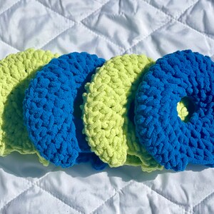 May include: Four crocheted hair scrunchies in a mix of blue and green colors. The scrunchies are made with a soft, fuzzy yarn.