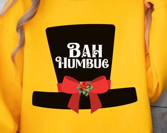 May include: A yellow sweatshirt featuring a black top hat design with a red bow and the words "BAH HUMBUG" in white. The design is centered on the front of the long-sleeved garment. The sweatshirt is a casual style.