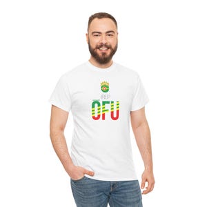 Könnte beinhalten: Weißes T-Shirt mit dem Text "I REP OFU" in Grün, Gelb und Rot. Das Design beinhaltet eine Krone über dem Text. Das T-Shirt wird von einer Person in Jeans getragen.
