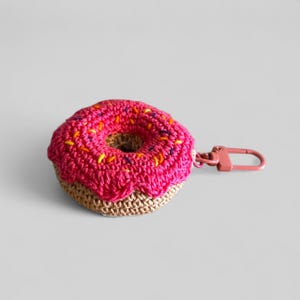 May include: A crocheted donut keychain with a pink frosting and colorful sprinkles. The donut base is tan, and the keychain hardware is pink. This handmade accessory is a fun and unique gift idea.