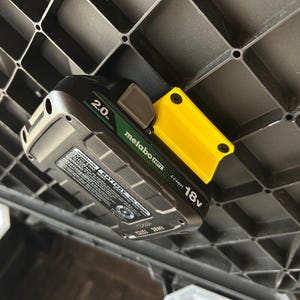 May include: A Metabo 18V Li-ion 2.0 battery pack with a yellow holder attached to a black plastic grid. The battery has green and black accents.