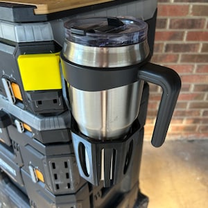 May include: A stainless steel travel mug with a black handle and lid sits in a black holder attached to a black and gray utility cart. The cart has yellow accents and a wooden top.