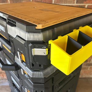 May include: A stack of black and gray toolboxes with a yellow organizer attached. The top toolbox has a wooden lid with a ruler printed on it. The organizer has two black dividers.
