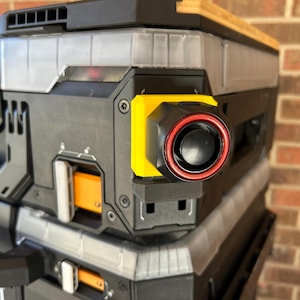 May include: Close-up of a black and gray toolbox with yellow and orange accents. The toolbox has a black circular component with a red ring. The word "BUILT" is visible on the side.