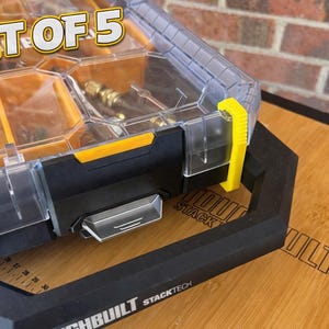 May include: A black and clear plastic storage container with yellow accents. The container has multiple compartments and a clear lid. The text "SET OF 5" is visible on the top. The container is on a wooden surface.