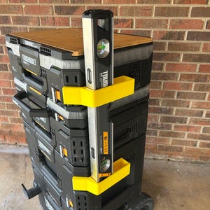 May include: A black and yellow rolling tool chest with a wooden top, holding a level. The level is black and silver with the text "TOUGH SERIES". The tool chest has multiple compartments and drawers.