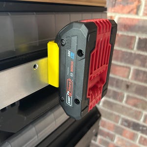 May include: A black and red 18V Bosch battery pack attached to a yellow bracket. The battery pack is labeled "18V 4.0 Ah" and "AMP Share". The bracket is mounted on a metal surface.