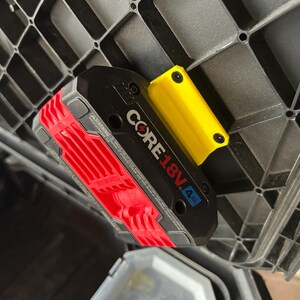 May include: A black and red CORE 18V 4 Ah battery pack with a yellow holder, mounted inside a black plastic storage container. The battery pack has the text "CORE 18V 4 Ah" printed on it.