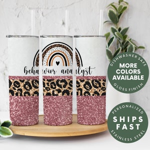 May include: Three stainless steel tumblers with a pink glitter bottom, a leopard print middle section, and a rainbow with a heart at the top. The tumblers have the text "behavior analyst" on them.