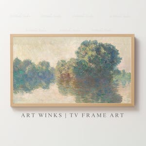 May include: A framed landscape painting featuring a serene waterscape with trees reflected in the water. The artwork uses a soft color palette of greens, blues, and browns, creating a tranquil and impressionistic scene. The frame is a light wood color.