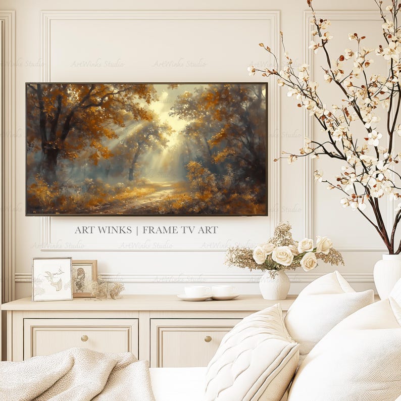 May include: A framed landscape art piece depicting a forest scene with golden-hued trees and sunlight streaming through the branches. The artwork is displayed above a white cabinet, with decorative elements like flowers and pillows.