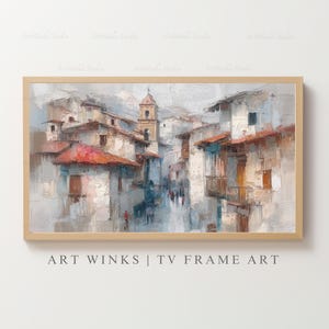 May include: An oil painting of a European village street scene, framed in a light wood. The buildings are white with red tile roofs, and a church steeple rises in the distance. The painting has a textured, impressionistic style.