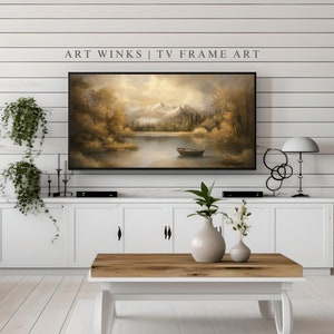 May include: A white living room with a white cabinet and a TV displaying a painting of a lake scene with mountains in the background. The TV is on a white cabinet with a black DVD player. There is a coffee table in front of the cabinet with a vase of flowers on it. There is a white couch on the left side of the image and a white chair on the right side of the image. The text "ART WINKS | TV FRAME ART" is displayed above the TV.
