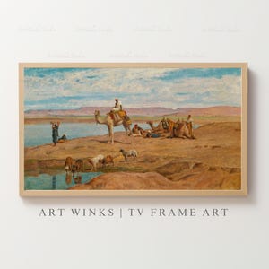 Puede incluir: Una impresión enmarcada de un paisaje desértico con camellos, figuras y ganado cerca de una masa de agua. La obra de arte presenta tonos cálidos de marrón, beige y azul, con un marco de madera clara. El texto "ART WINKS | TV FRAME ART" es visible en la parte inferior.