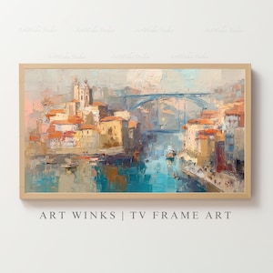 May include: Oil painting of a European cityscape with a bridge, buildings, and water. The artwork is framed in a light wood frame. The color palette includes blues, oranges, and beige. The text "ART WINKS | TV FRAME ART" is at the bottom.