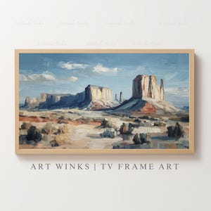 May include: A framed landscape painting of a desert scene with large rock formations under a blue sky with white clouds. The painting has a light brown wooden frame. The text "ART WINKS | TV FRAME ART" is at the bottom of the frame.