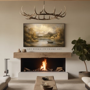 May include: A living room interior with a fireplace, a large TV screen displaying a landscape painting, a wooden mantel, and a potted plant. The painting depicts a lake with mountains in the background and a small boat on the water. The text "ART WINKS | TV FRAME ART" is displayed below the painting.