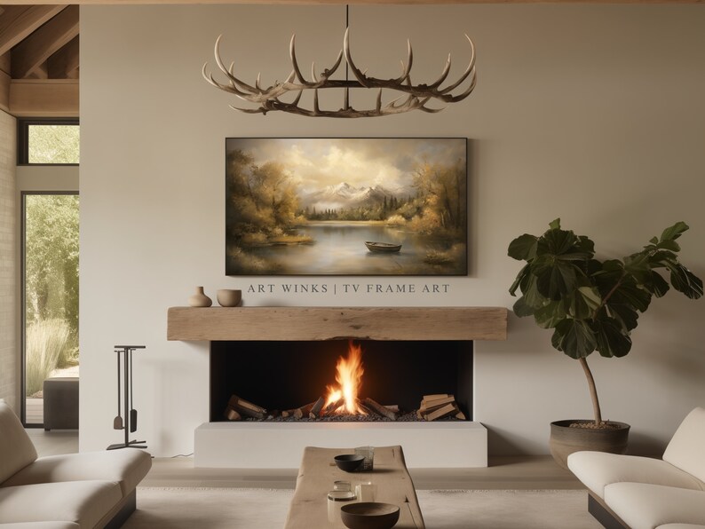 May include: A living room interior with a fireplace, a large TV screen displaying a landscape painting, a wooden mantel, and a potted plant. The painting depicts a lake with mountains in the background and a small boat on the water. The text "ART WINKS | TV FRAME ART" is displayed below the painting.