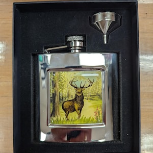May include: A silver flask with a stag design in a black velvet box. The flask has a funnel and a hinged cap.