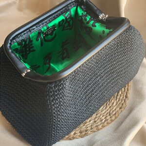 May include: A black crocheted clutch purse with a green satin lining. The lining features black Chinese characters and the word "Cozy" in white.