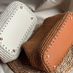 May include: Two crocheted bags with leather bottoms. One bag is white and the other is brown.