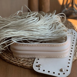 May include: A white leather bag kit with a woven base and a pile of white cord. The bag kit has a flap with a row of holes and a metal rivet.