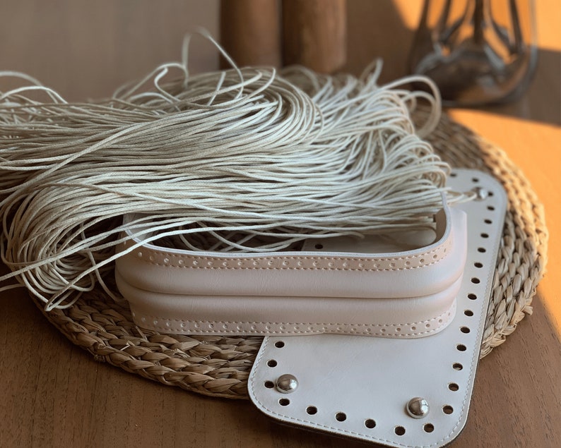 May include: A white leather bag kit with a woven base and a pile of white cord. The bag kit has a flap with a row of holes and a metal rivet.